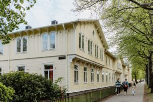 Hörnvy av gul trävilla på Barnarpsgatan 39 med människor som promenerar.